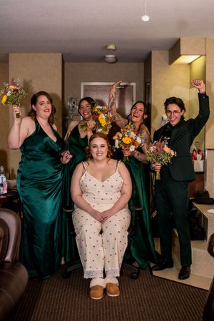 Wedding party celebration scene with people in emerald green dresses and suits holding colorful floral bouquets.