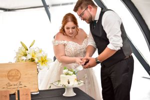A couple in formal wedding attire cuts their rustic wooden cake together at their reception celebration.
