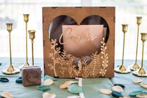Decorative wooden wedding card box with heart cutout surrounded by gold candlesticks on a blue tablecloth.