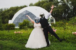 Wedding couple poses on grass with white geodesic dome structure visible in background.