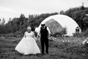 A black and white panoramic view of a wedding ceremony with geodesic domes in the background.