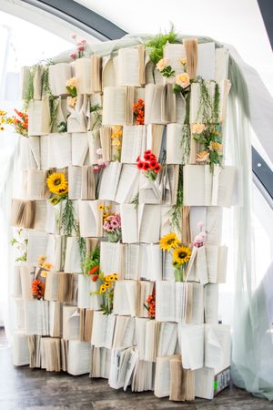 Creative wedding backdrop made from open books and fresh flowers arranged in a geometric pattern.
