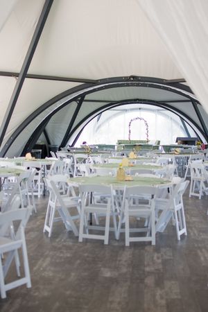 White folding chairs arranged in rows under a large white tent for an outdoor wedding ceremony.