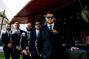Groomsmen in dark suits and sunglasses pose together outdoors.
