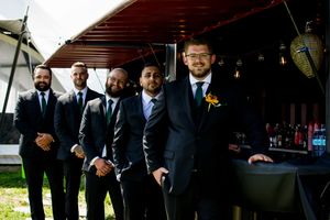 Groomsmen in dark suits posing together outdoors.