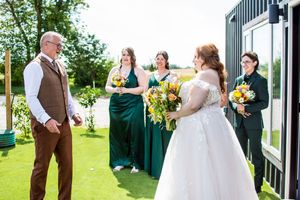 Wedding party members in brown and green attire pose together outdoors on a sunny day.