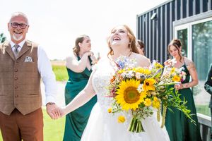 Wedding party celebrates outdoors with bright sunflower bouquets and emerald green attire.