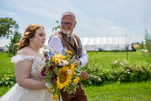 Wedding party holding vibrant sunflower bouquets poses in a sunny outdoor field.