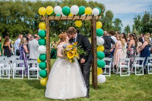 Outdoor wedding ceremony setup with green and yellow balloon arch decorations on a sunny day.