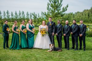 Wedding party poses outdoors in emerald green dresses and dark suits against a natural landscape backdrop.