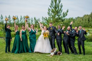 Wedding party poses outdoors with bridesmaids in green dresses and groomsmen in black suits.
