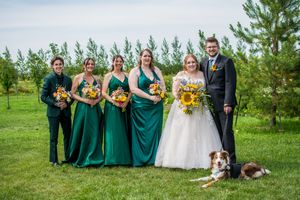 Wedding party relaxes on grassy lawn with evergreen trees in background.