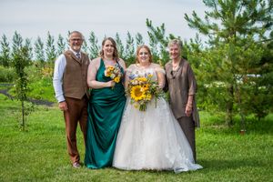 Small wedding group poses together outdoors with pine trees in the background.