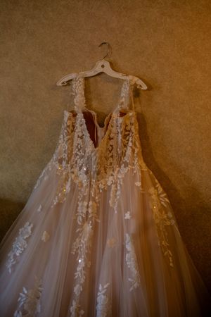 Elegant white wedding dress with delicate lace appliques hanging on display.