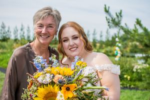 Wedding couple poses with sunflower bouquets in outdoor garden setting.
