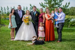 Wedding party poses for group photos outdoors on a sunny day with green grass and trees in the background.
