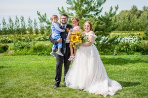 Wedding party poses in a sunny outdoor garden setting with green trees and grass in the background.