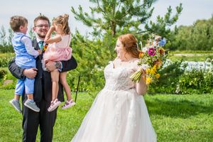 Wedding party gathers outdoors on a sunny day with evergreen trees and colorful wildflower bouquets.