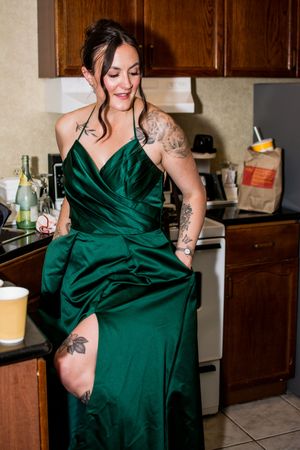 Woman in emerald green silk dress poses in kitchen showing off the flowing fabric.