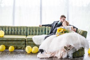 Wedding party lounges on vintage green velvet couch in bright white room.