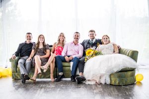 A group relaxes together on a vintage green couch with yellow balloons and white curtains in the background.