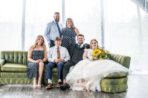 Wedding group relaxes casually on antique green couch with yellow balloons.