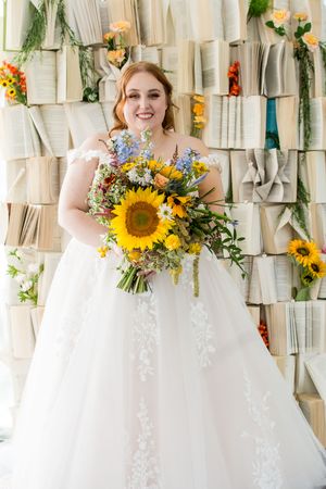 A beautiful wedding bouquet with vibrant sunflowers and white flowers against a textured fabric backdrop.