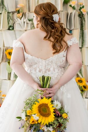 Back view of a bride in a lace wedding dress holding a vibrant sunflower bouquet.