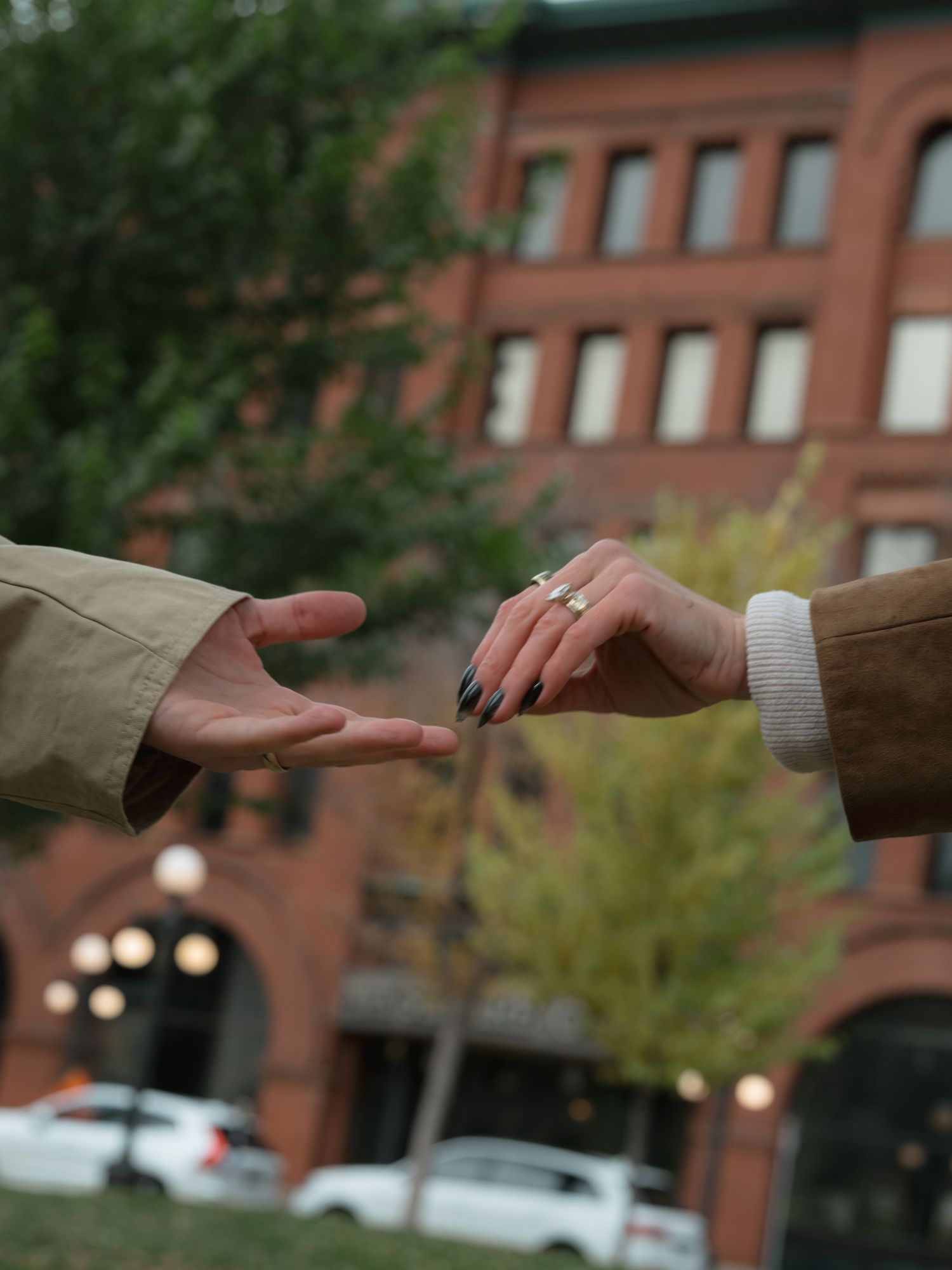 Two hands reaching towards each other against a blurred brick building background with street lamps.