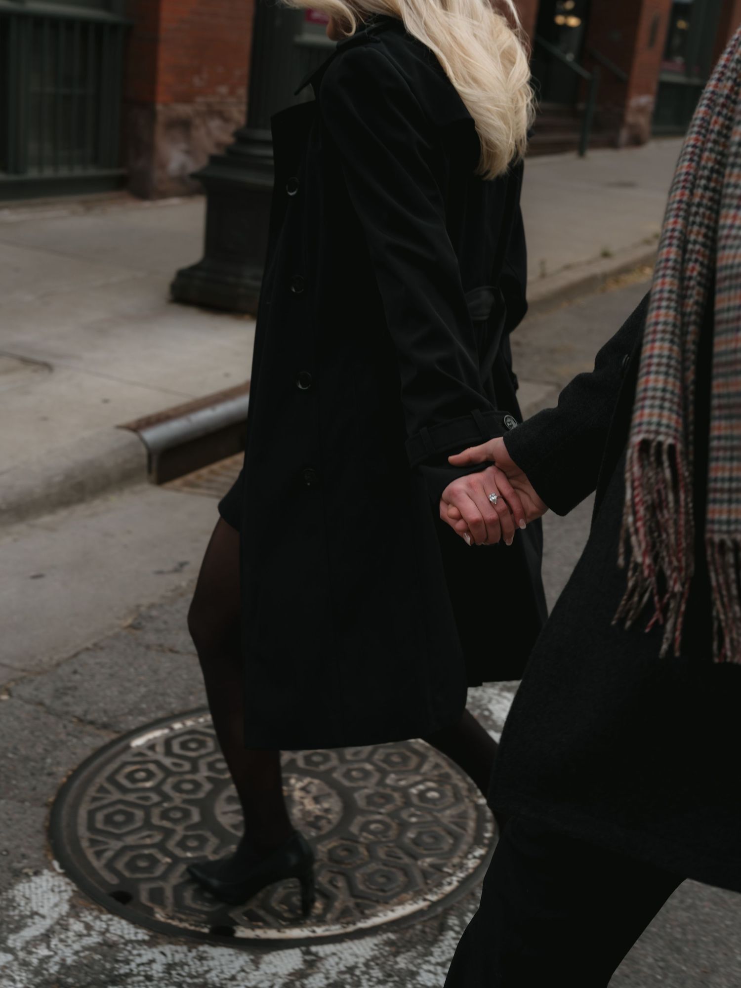 Couple holding hands while walking on urban sidewalk with decorative manhole cover pattern visible.