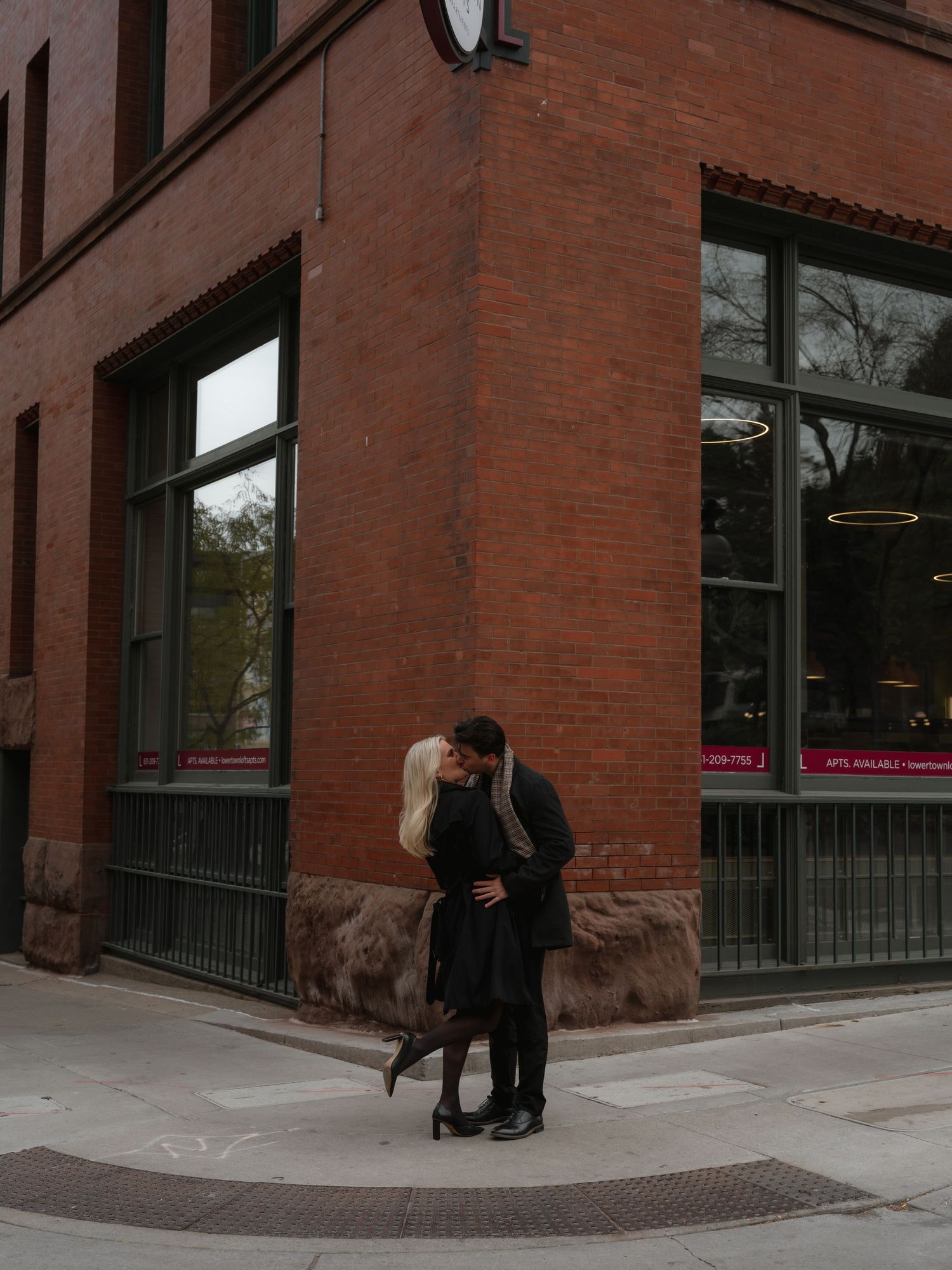 People walking past a red brick building corner with large windows and a curved entrance on a city street.