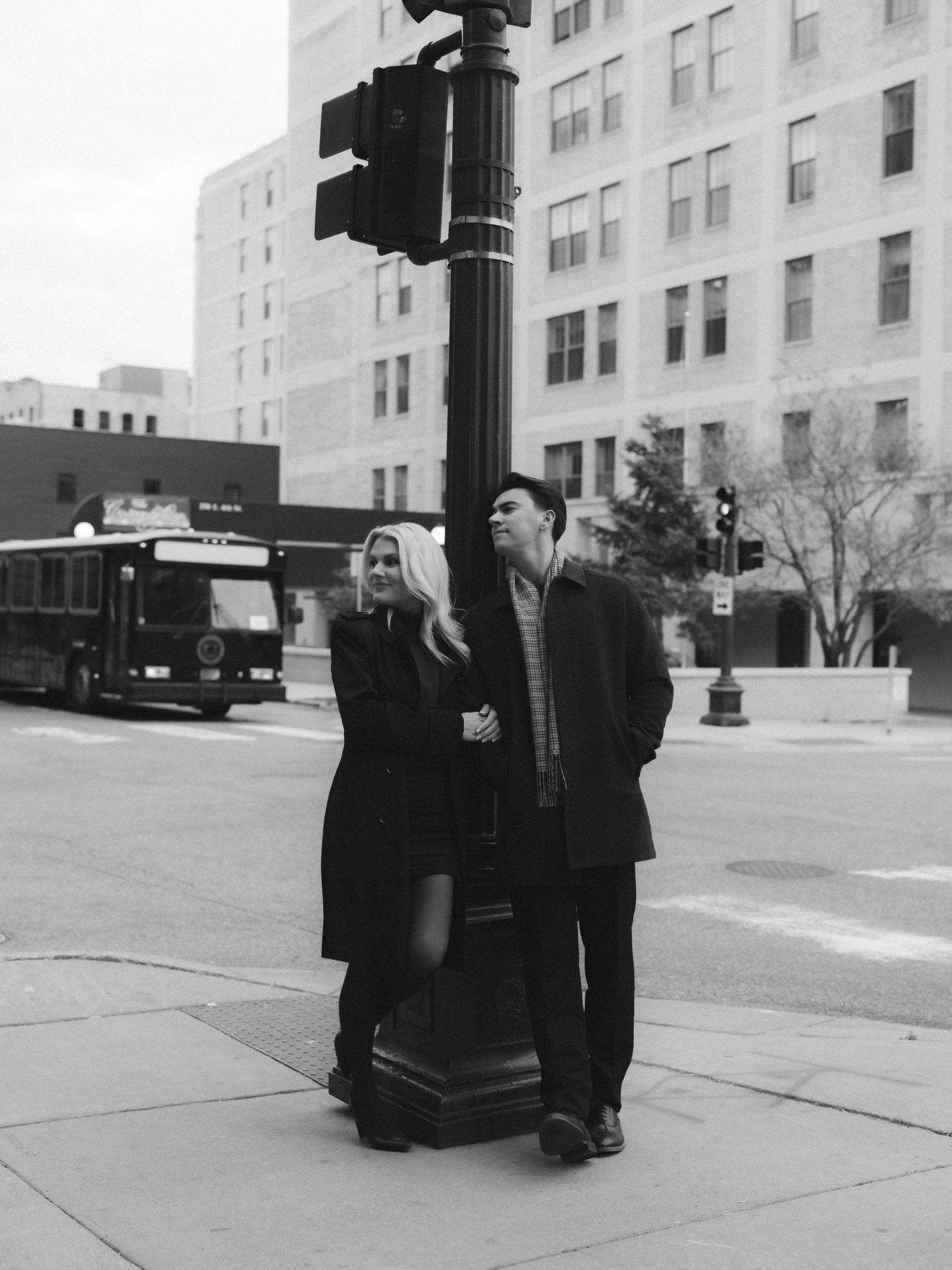 A black and white photo series showing two people standing near a utility pole on an urban street with buildings.