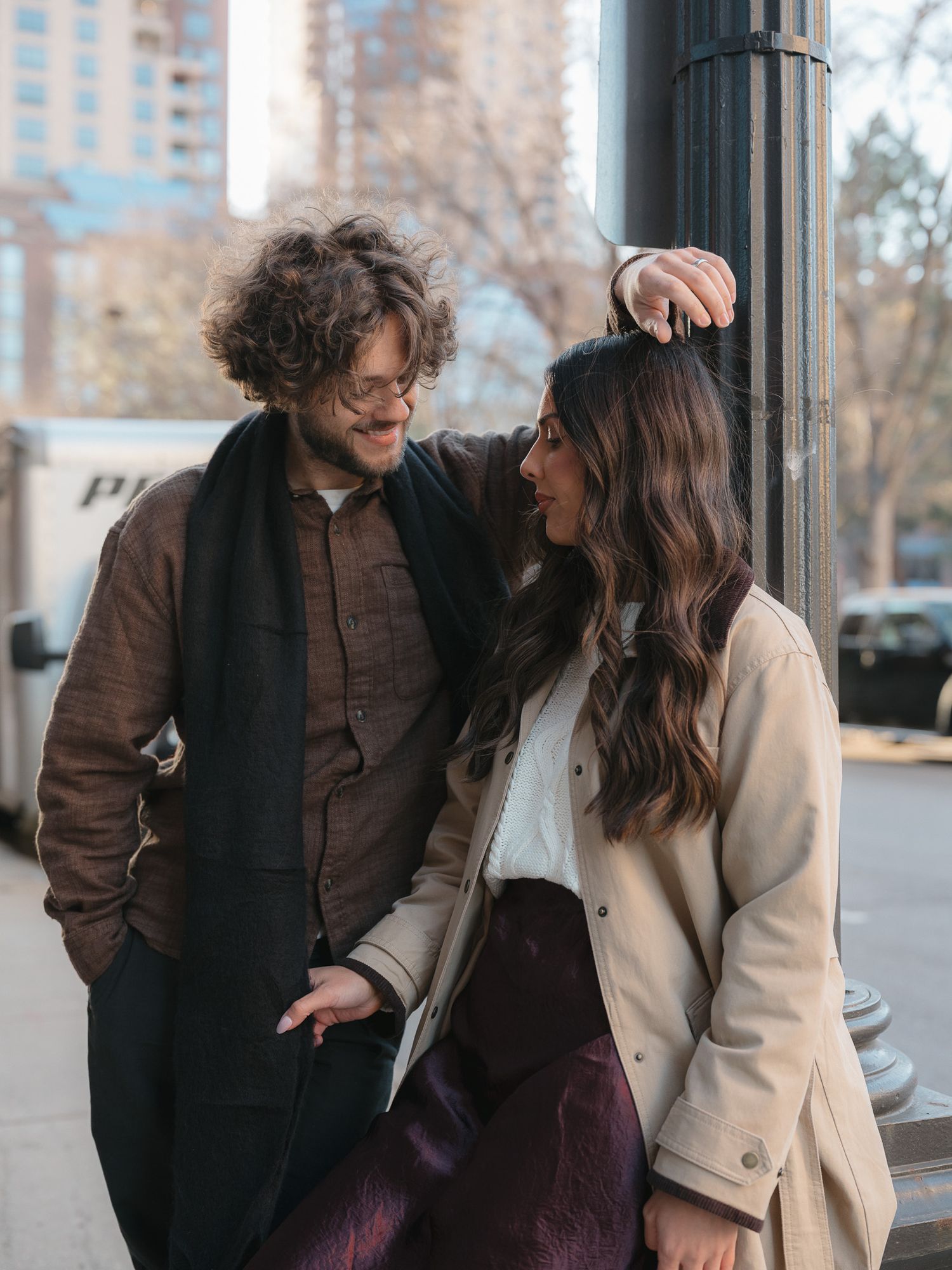 A couple shares a joyful moment while sitting on a bench in an urban setting on a winter day.
