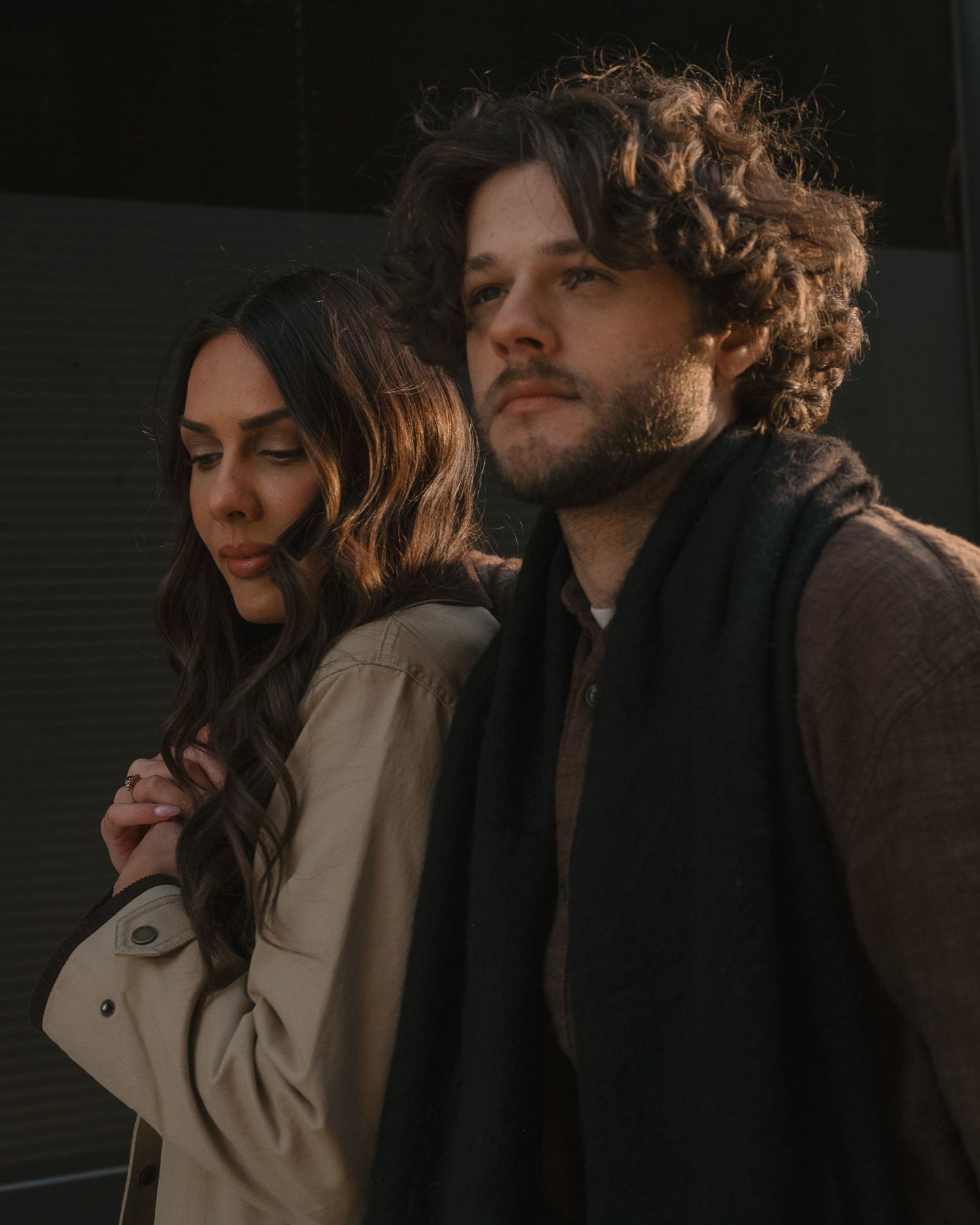 A couple in casual attire share an intimate moment while standing close together in dim lighting.