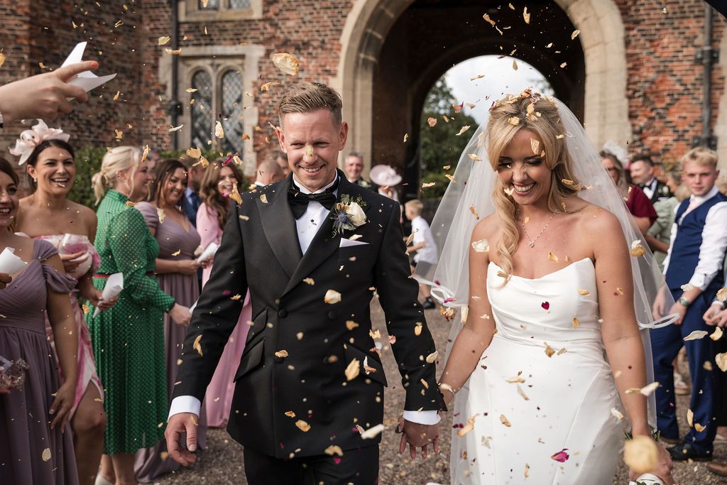 Wedding guests throwing confetti in front of the Gatehouse at Hodsock Priory as the bride and groom smile