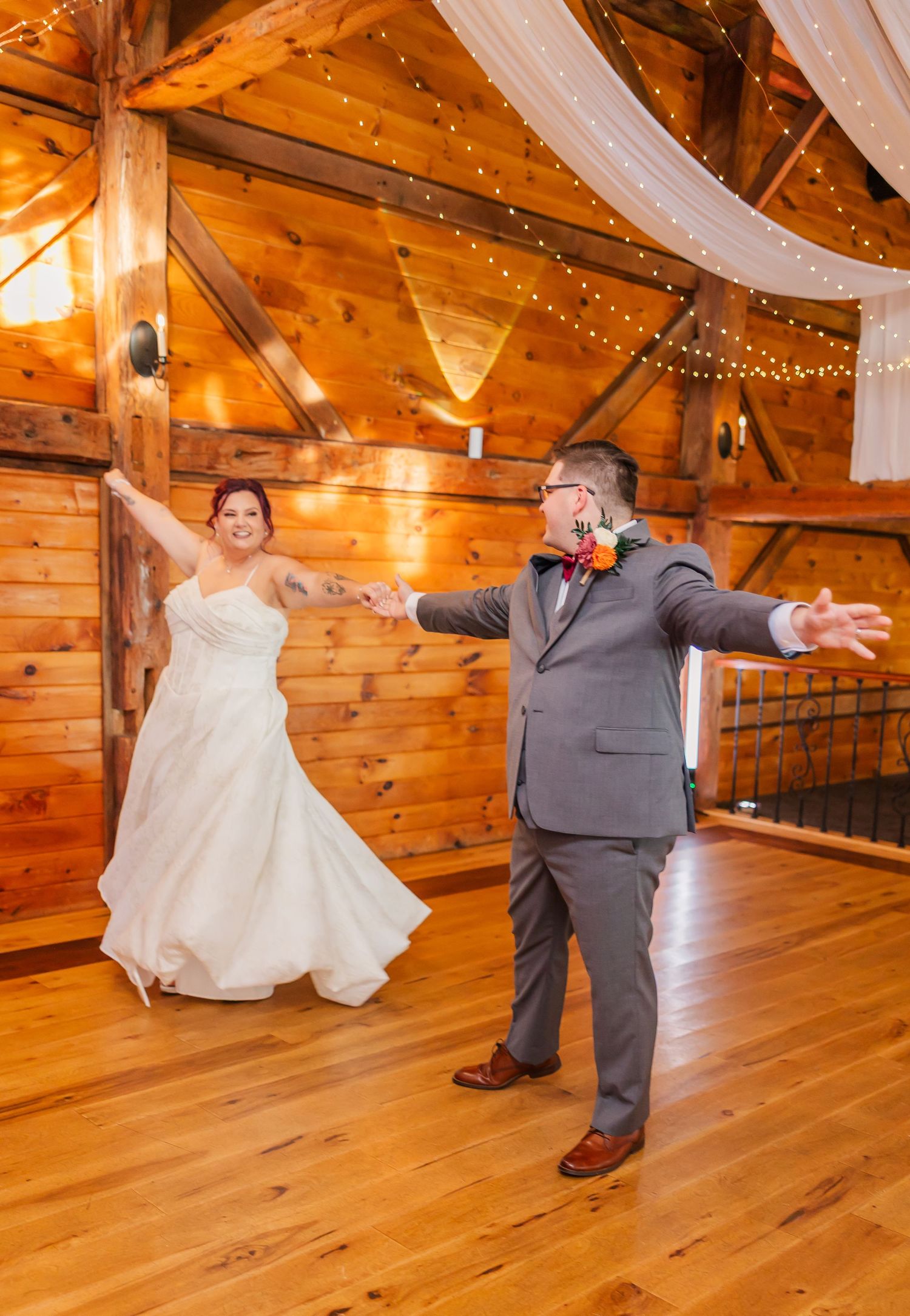 A wedding celebration in a rustic wooden barn venue decorated with string lights and white fabric draping.