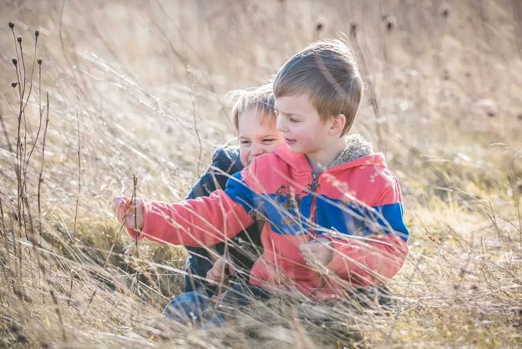 Two young brothers sitting in a dry grassy field, laughing and playing together.