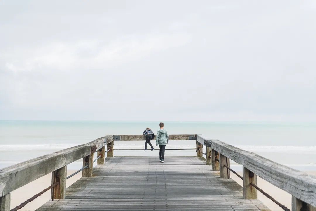 Family walking along a wooden pier beside a calm, misty sea.
