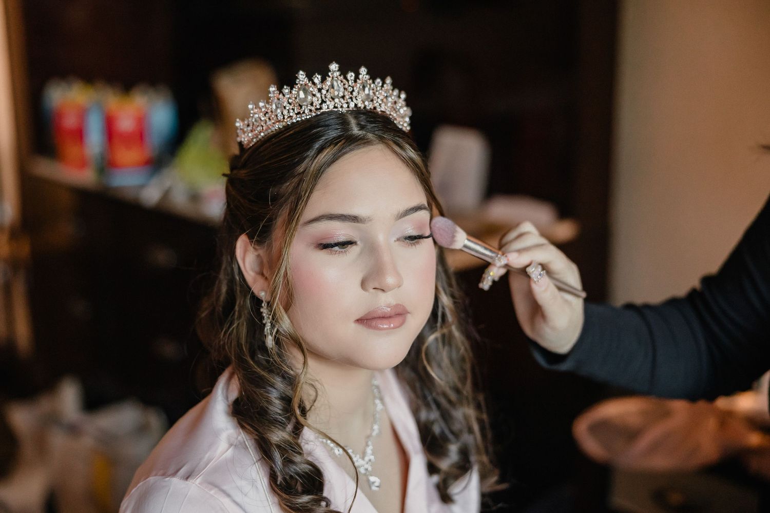 Professional makeup artist applies finishing touches to a pink gown and tiara ensemble during preparation.