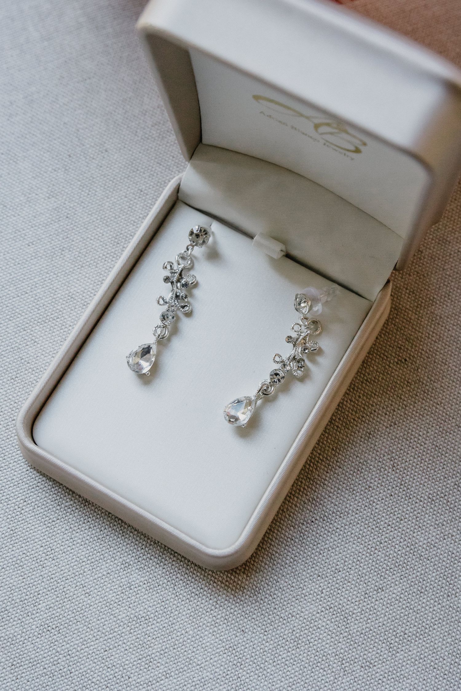 Delicate crystal drop earrings displayed in white jewelry boxes showing different angles and details.