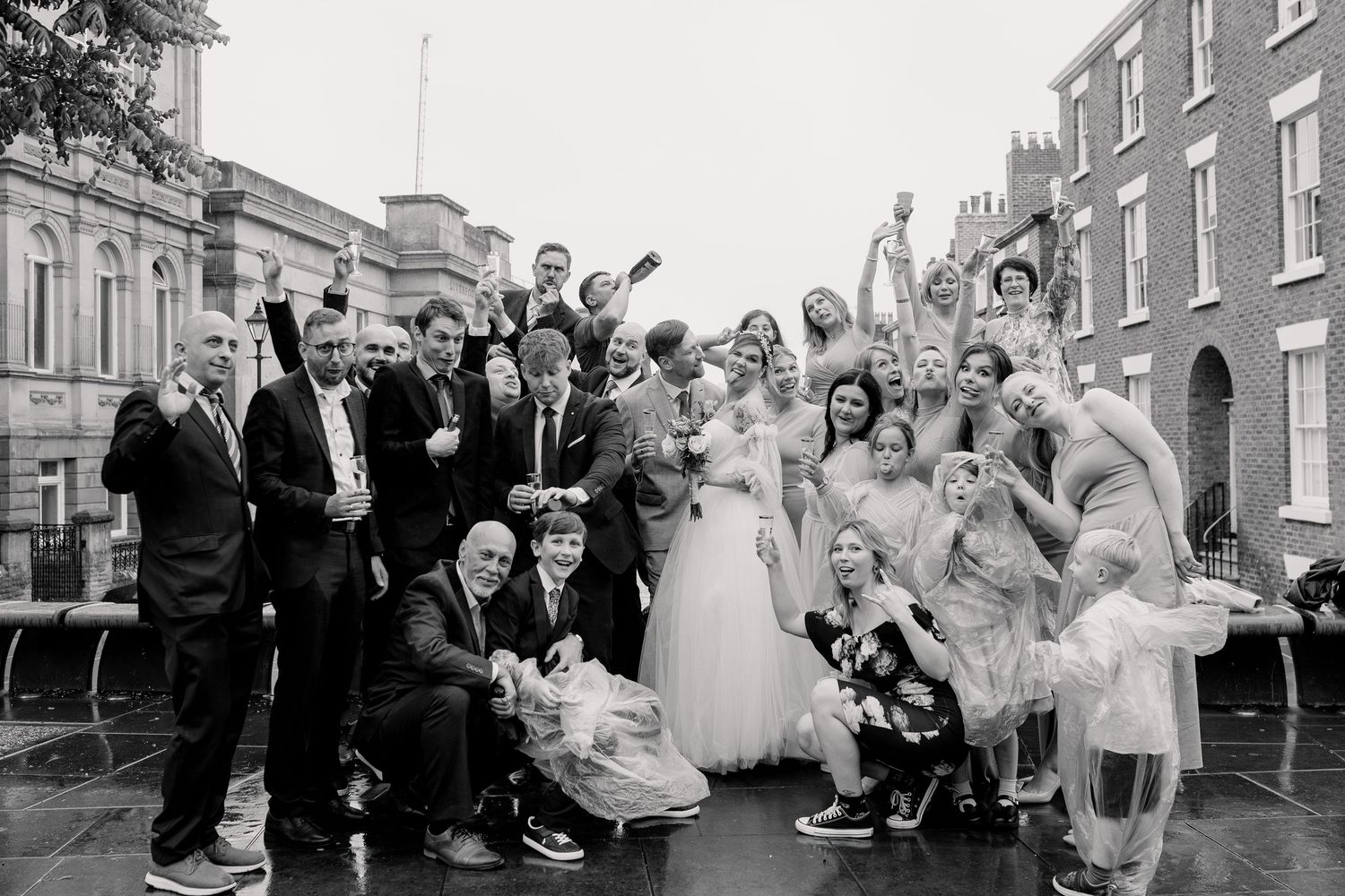 A black and white wedding party photo showing a large group celebrating together on a city street.