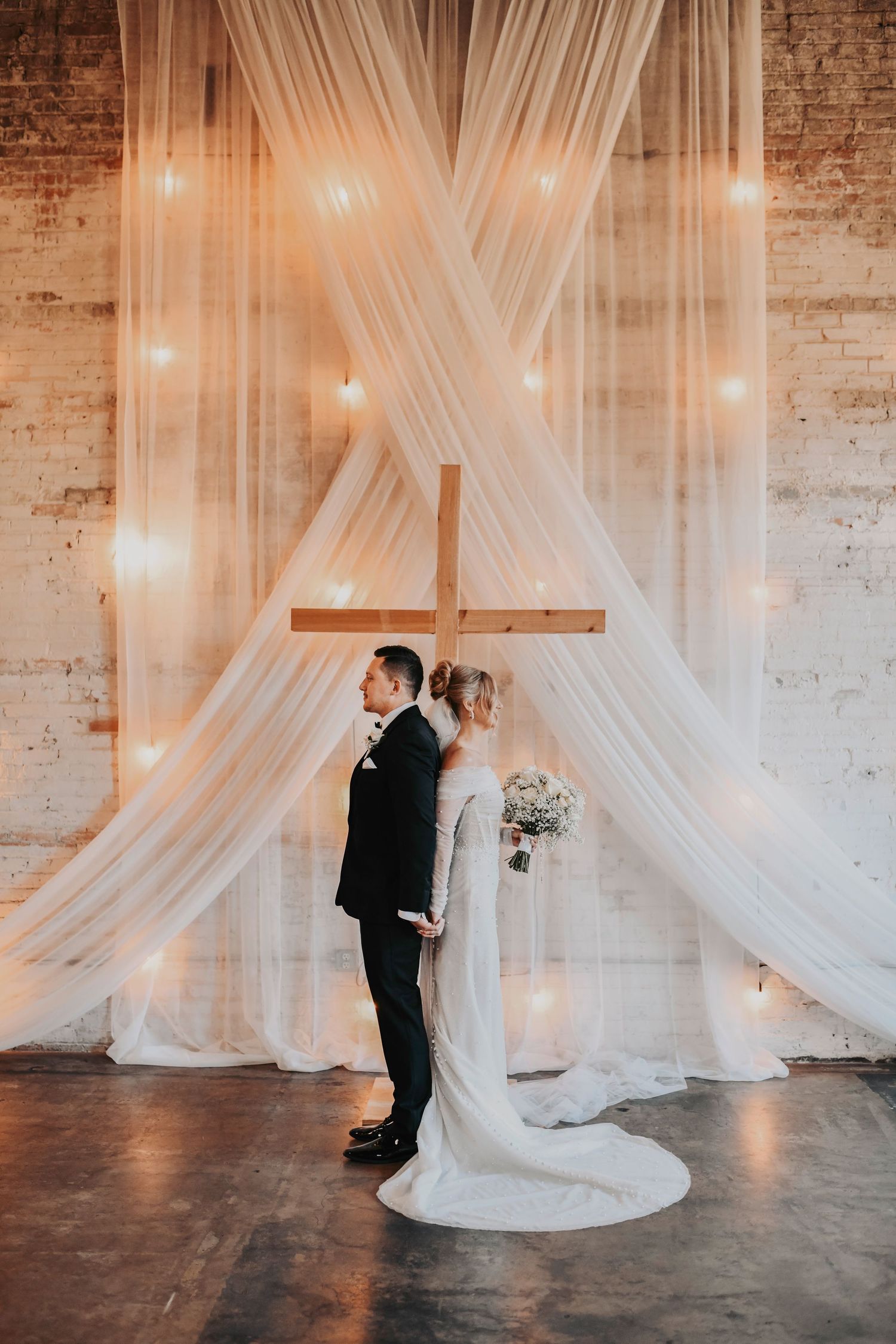 Bride and groom bow their heads in prayer, sharing a sacred moment of faith during their modern wedding at Brake & Clutch Warehouse.