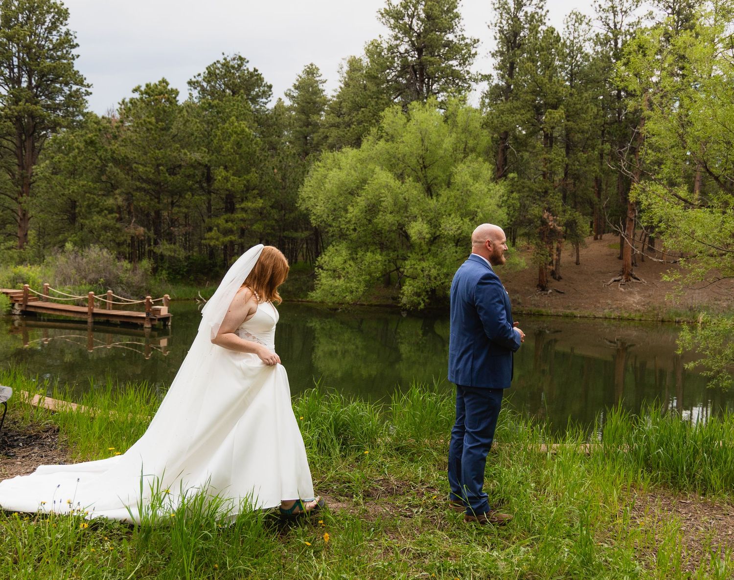 A romantic outdoor wedding photoshoot by a serene lake with lush greenery and trees in the background.