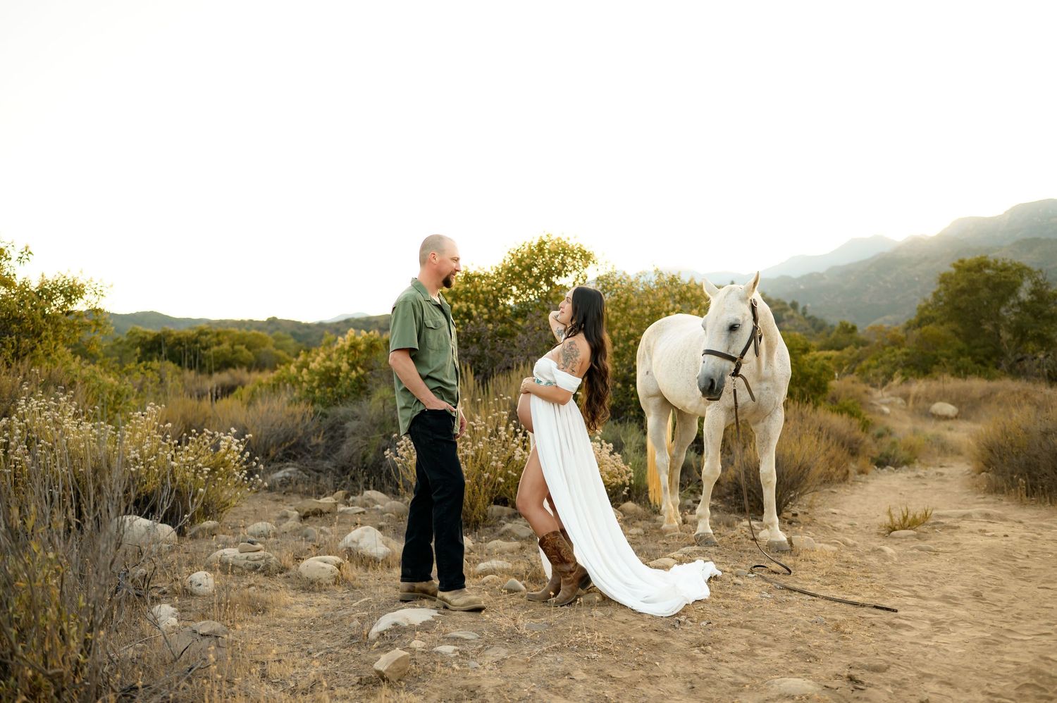 couple stands with horse in Ojai preserve during their cowboy maternity photoshoot by Ojai, Ventura Photographer