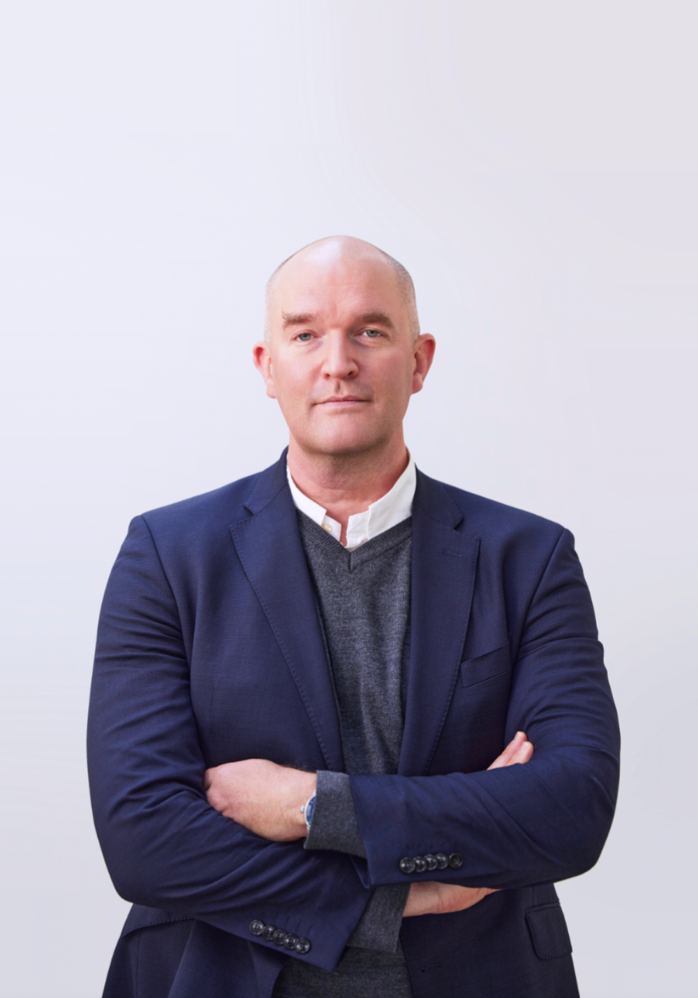 Professional wearing a navy blazer and gray sweater poses with arms crossed against white background.