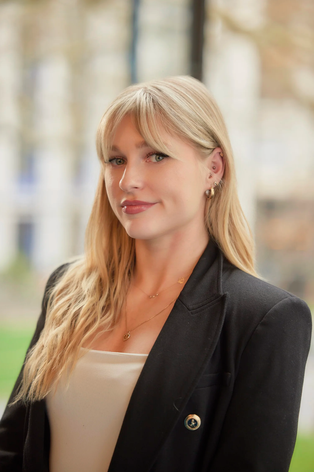 Professional portrait of person in black blazer and beige top with long blonde hair.