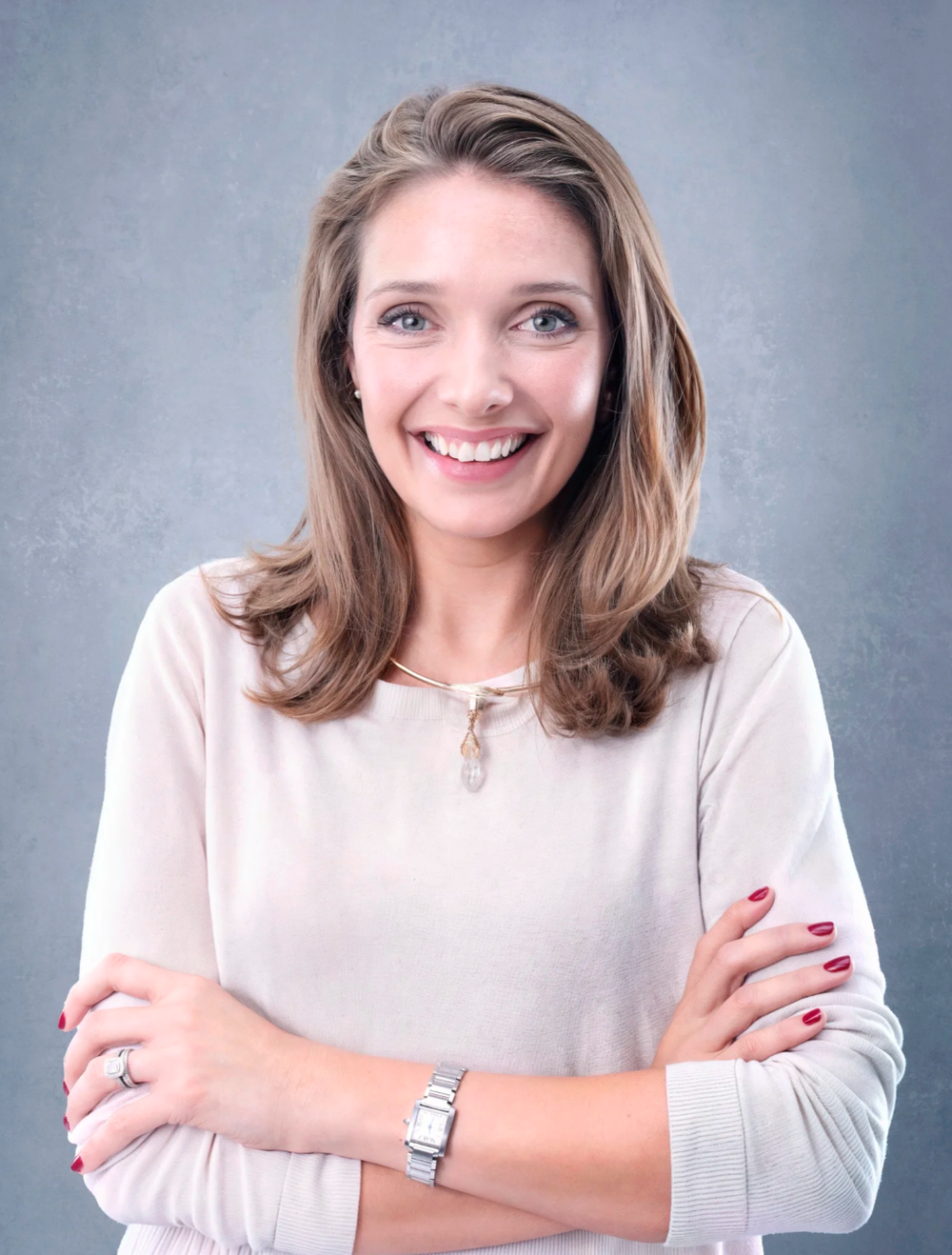 Professional headshot of person in white sweater with crossed arms and warm smile.