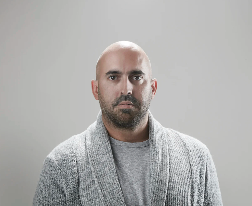 Studio portrait of someone in a grey cardigan against a light background.