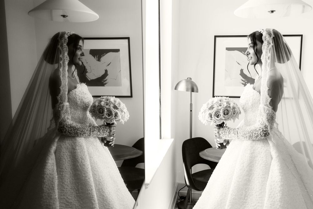 Black and white photo of a bride in a strapless gown holding a bouquet, reflected in a mirror.