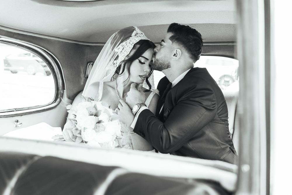 Black and white photo of a bride and groom sharing an intimate moment inside a vintage car on their wedding day.